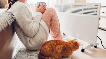 Pessoa com os pés estendidos em cima de um radiador de parede. Os pés têm meias calçadas. Ao lado há um móvel, em cima do qual está uma caneca de chá.