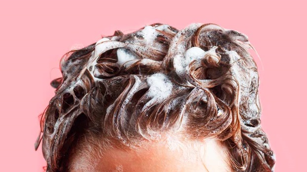 Grande plano do topo de uma cabeça de mulher a lavar o cabelo com champô, fundo cor-de-rosa